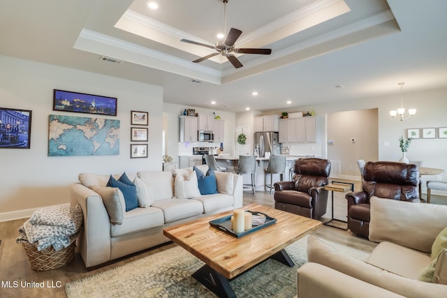 living room with ornamental molding, a tray ceiling, ceiling fan with notable chandelier, and light wood-type flooring