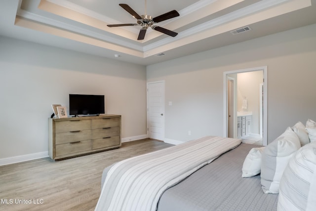 bedroom with light wood-type flooring, ceiling fan, a tray ceiling, crown molding, and ensuite bath