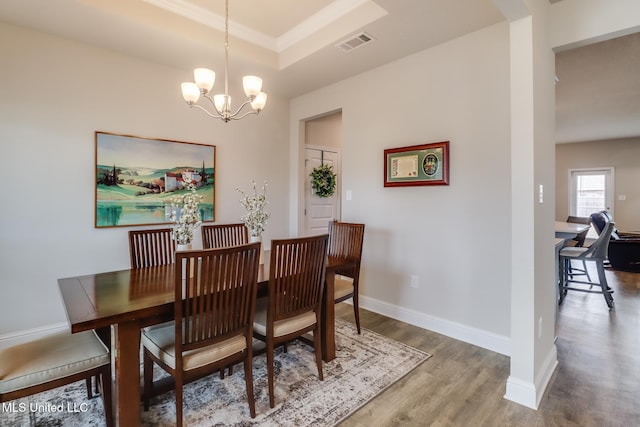 dining space with hardwood / wood-style flooring, a tray ceiling, and an inviting chandelier