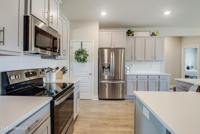 kitchen featuring stainless steel appliances, white cabinets, light hardwood / wood-style floors, and decorative backsplash