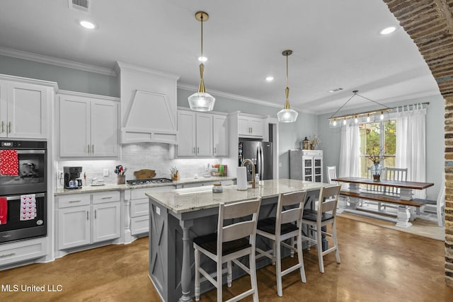 kitchen with premium range hood, a center island with sink, and white cabinets