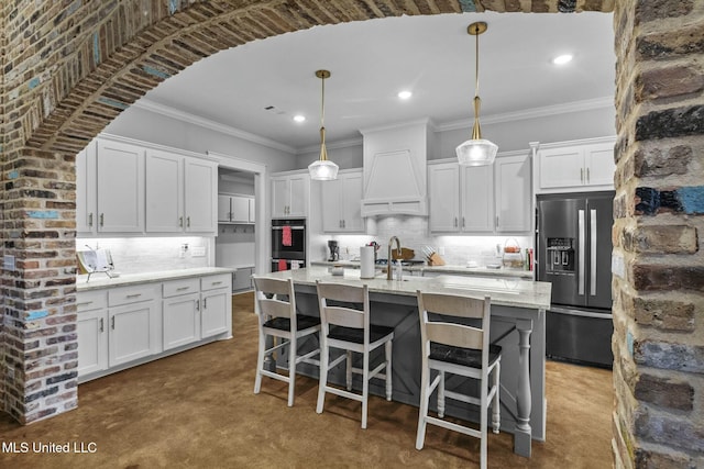 kitchen featuring decorative light fixtures, white cabinetry, an island with sink, crown molding, and fridge with ice dispenser