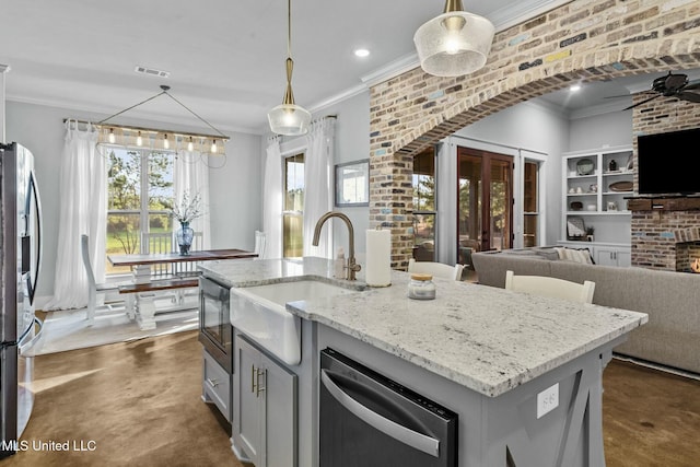 kitchen featuring sink, hanging light fixtures, stainless steel appliances, light stone countertops, and a center island with sink