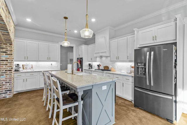 kitchen featuring a breakfast bar, appliances with stainless steel finishes, white cabinetry, hanging light fixtures, and a kitchen island with sink