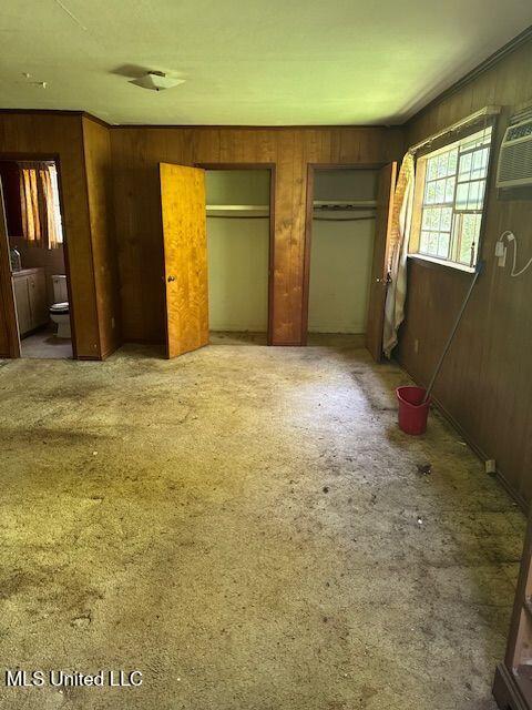 3411 25th Ave, Meridian, MS 39305 - unfurnished bedroom featuring wood walls, connected bathroom, and multiple closets