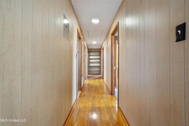 corridor with wood walls, light wood-type flooring, and a textured ceiling