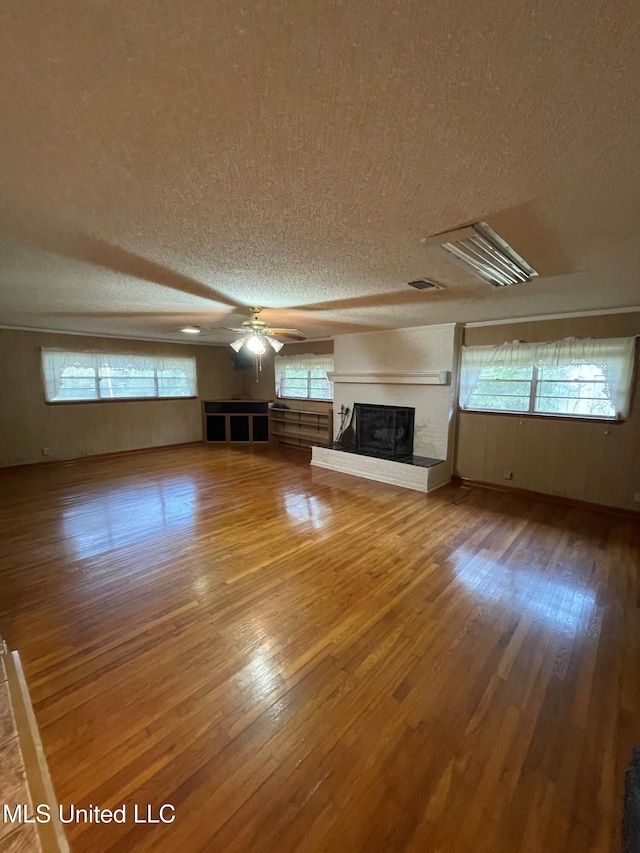 unfurnished living room with wood-type flooring, a textured ceiling, a brick fireplace, and ceiling fan