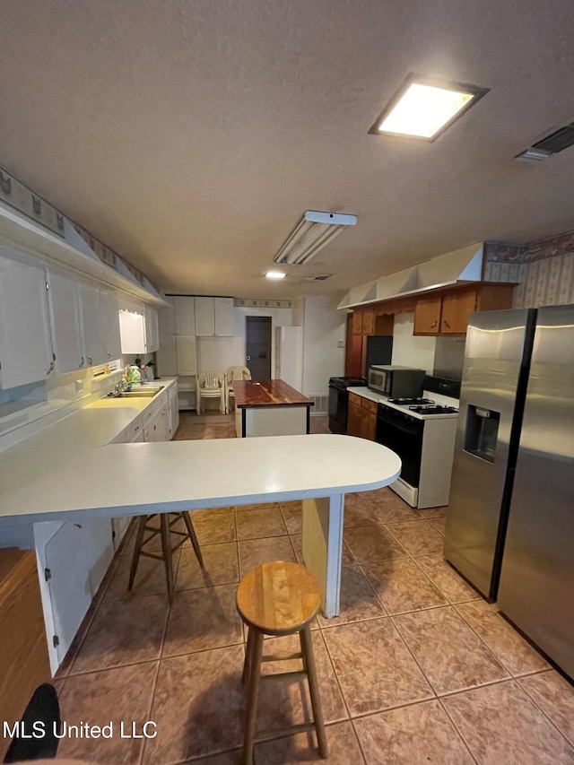 kitchen featuring kitchen peninsula, appliances with stainless steel finishes, a breakfast bar, light tile patterned floors, and white cabinetry