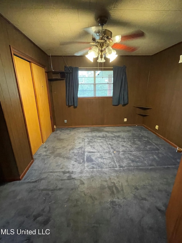 unfurnished bedroom with ceiling fan, wooden walls, and a closet