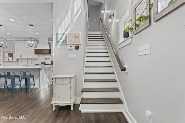 stairway featuring baseboards, a notable chandelier, wood finished floors, and recessed lighting