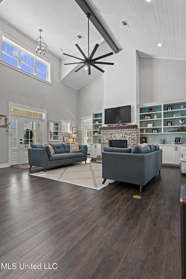 living area with visible vents, beamed ceiling, a fireplace, ceiling fan with notable chandelier, and dark wood-style floors