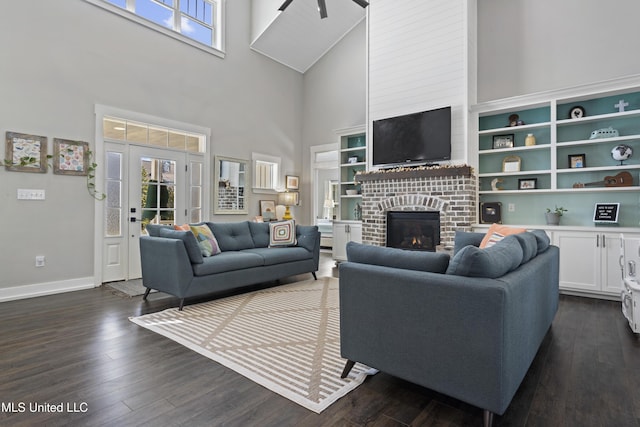 living room featuring dark wood-style floors, a fireplace, a towering ceiling, and baseboards
