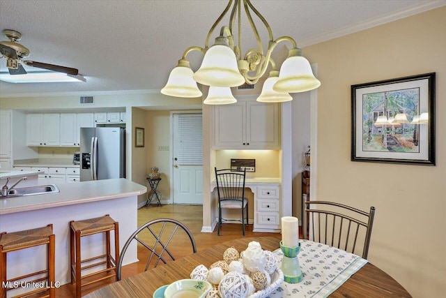 dining space with sink, built in desk, a textured ceiling, ornamental molding, and light hardwood / wood-style floors