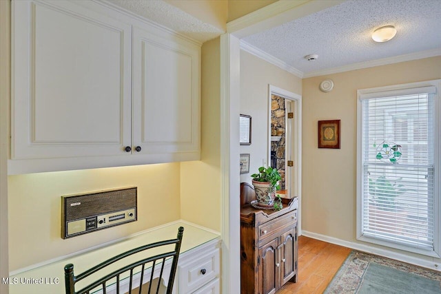 kitchen featuring white cabinets, ornamental molding, light hardwood / wood-style floors, and a textured ceiling