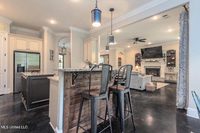 kitchen with light stone countertops, stainless steel fridge, a fireplace, a ceiling fan, and visible vents