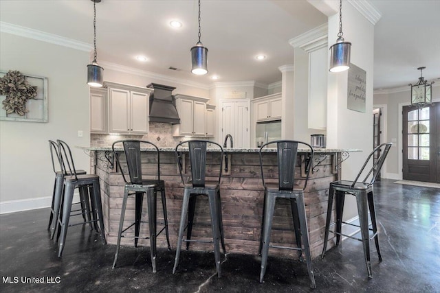 kitchen featuring a peninsula, baseboards, stainless steel refrigerator with ice dispenser, tasteful backsplash, and custom range hood
