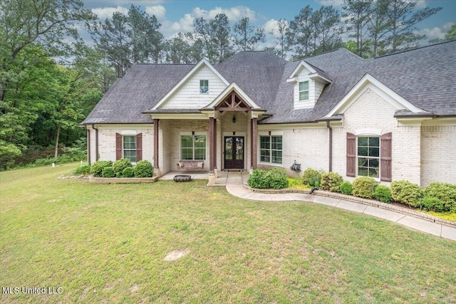 view of front of house with brick siding, french doors, a front yard, and roof with shingles