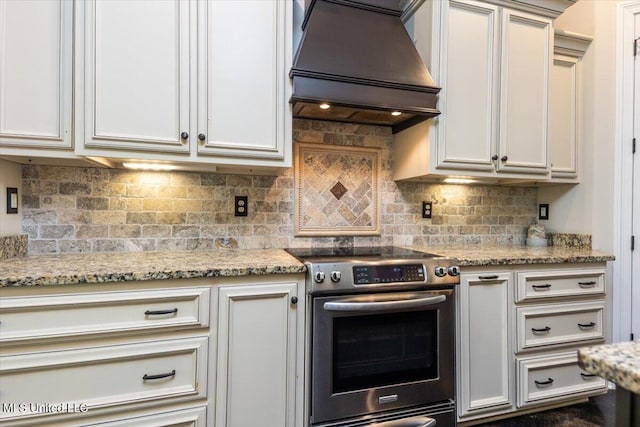 kitchen with stainless steel electric range oven, backsplash, custom exhaust hood, and light stone counters