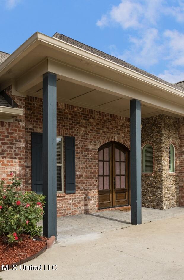 219 Bellamy Ct, Flowood, MS 39232 - doorway to property with brick siding, covered porch, and roof with shingles