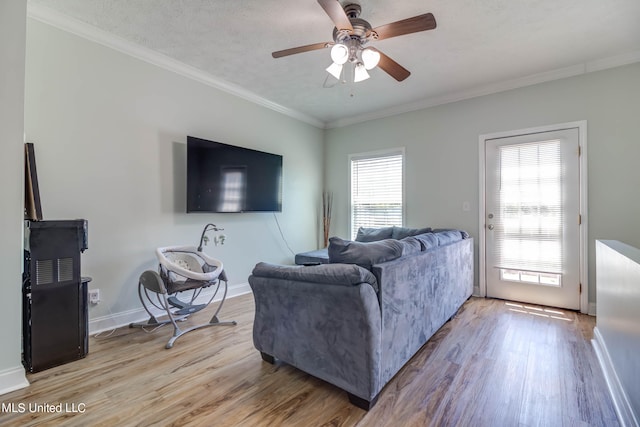 living room featuring light hardwood / wood-style flooring, ceiling fan, crown molding, and a wealth of natural light