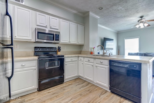 kitchen with kitchen peninsula, ornamental molding, sink, black appliances, and white cabinets