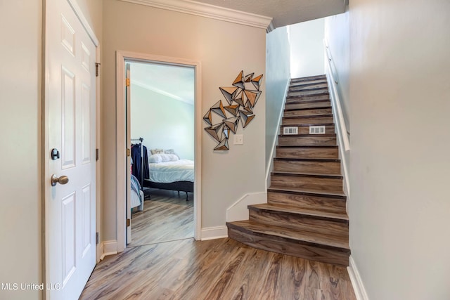 staircase with hardwood / wood-style floors and crown molding