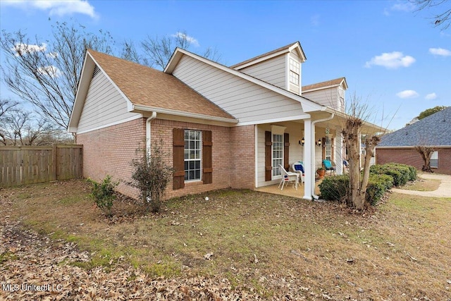 view of front of property featuring a shingled roof, a patio area, brick siding, and fence