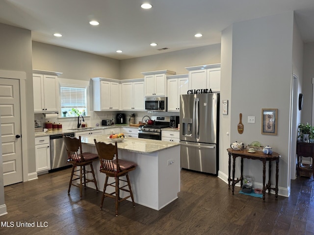 kitchen featuring a kitchen island, dark wood-type flooring, white cabinets, appliances with stainless steel finishes, and light stone counters