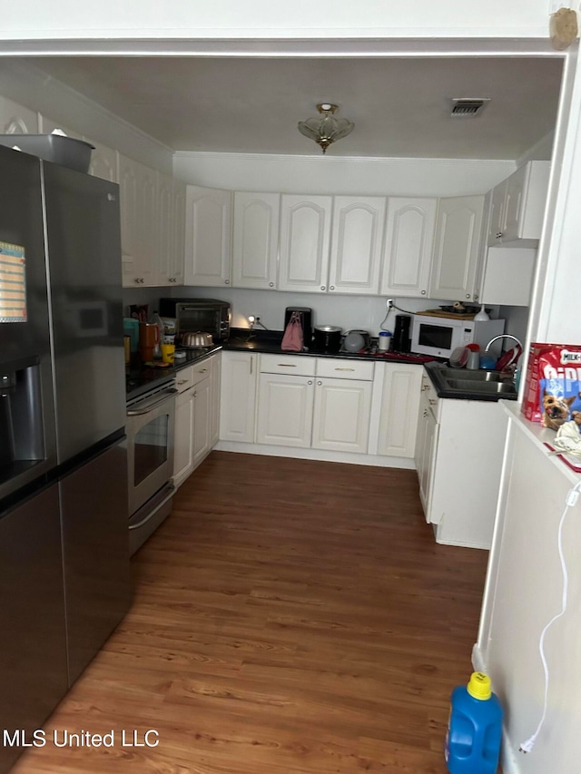 kitchen featuring dark wood-type flooring, stainless steel stove, refrigerator with ice dispenser, and white cabinets