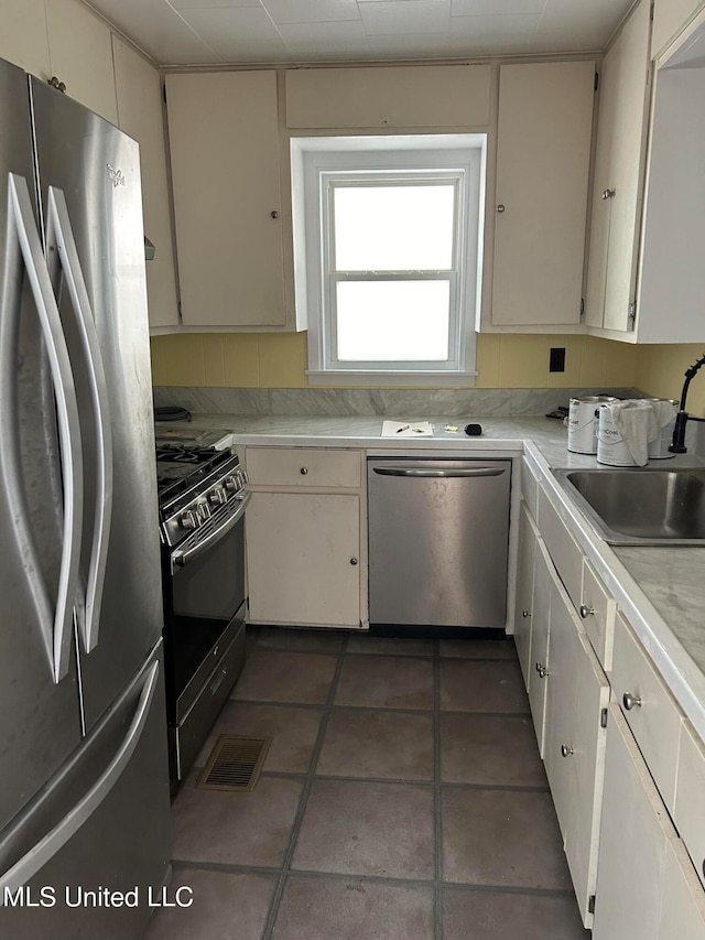 kitchen with dark tile patterned floors, sink, white cabinets, and stainless steel appliances