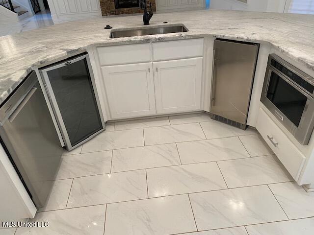 kitchen featuring stainless steel appliances, light stone countertops, white cabinetry, and sink