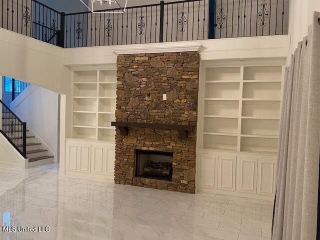 unfurnished living room with a stone fireplace, a towering ceiling, and built in features