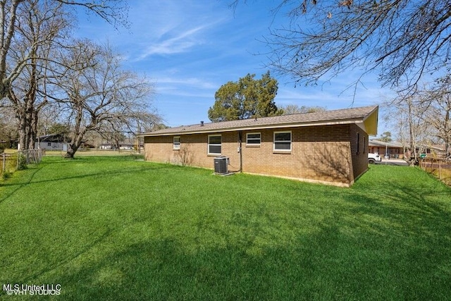 rear view of house with brick siding, central air condition unit, a lawn, and fence