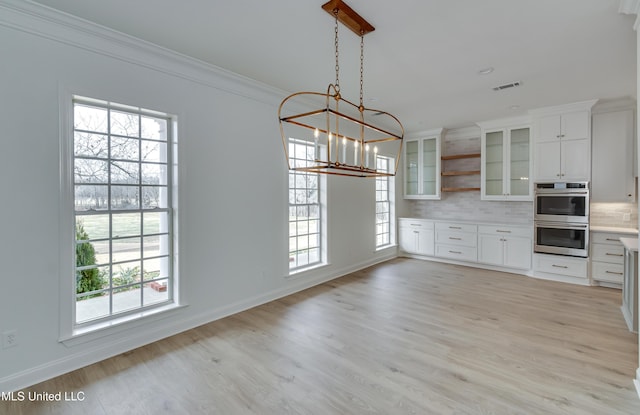 kitchen with light hardwood / wood-style floors, crown molding, decorative backsplash, white cabinetry, and decorative light fixtures