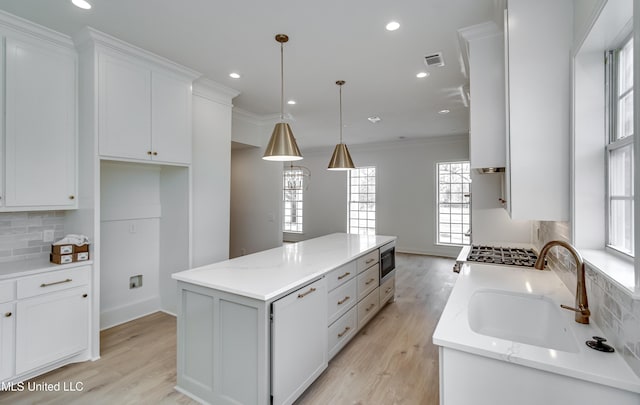 kitchen with light stone countertops, hanging light fixtures, decorative backsplash, a kitchen island, and white cabinetry