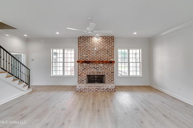 unfurnished living room featuring a brick fireplace, ceiling fan, light hardwood / wood-style floors, and crown molding