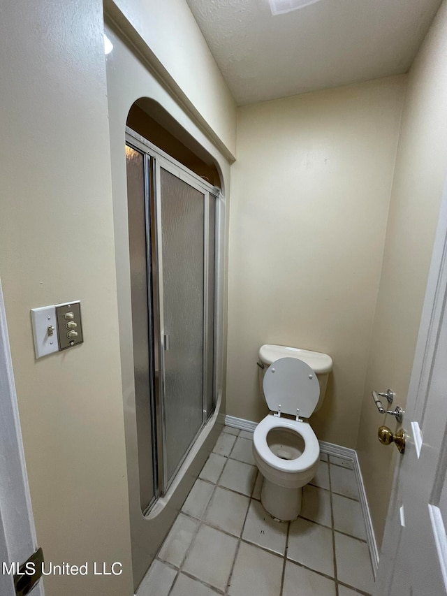 bathroom featuring toilet, a shower with shower door, and tile patterned floors