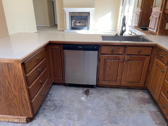 kitchen with kitchen peninsula, a tiled fireplace, tile countertops, stainless steel dishwasher, and sink