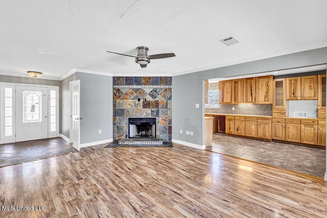 unfurnished living room featuring ornamental molding, a stone fireplace, a wealth of natural light, and light hardwood / wood-style floors