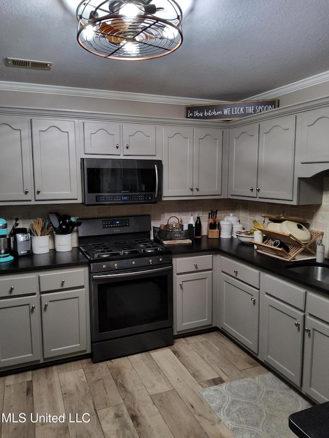 kitchen with visible vents, ornamental molding, dark countertops, light wood-style floors, and appliances with stainless steel finishes