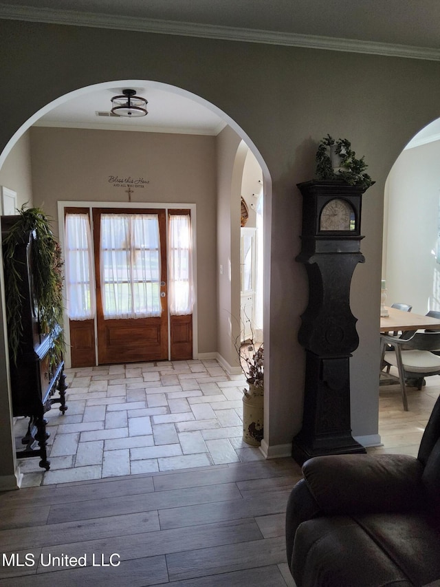 foyer entrance with crown molding, wood finished floors, arched walkways, and baseboards