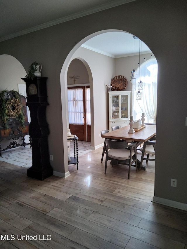 dining space featuring baseboards, arched walkways, wood finished floors, and crown molding