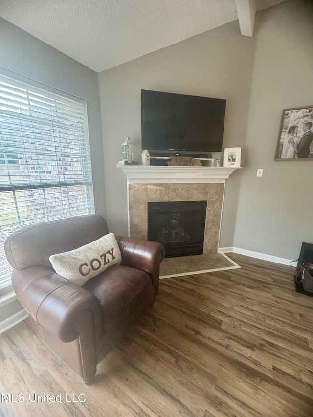 living room featuring vaulted ceiling, a fireplace, wood finished floors, and a textured ceiling