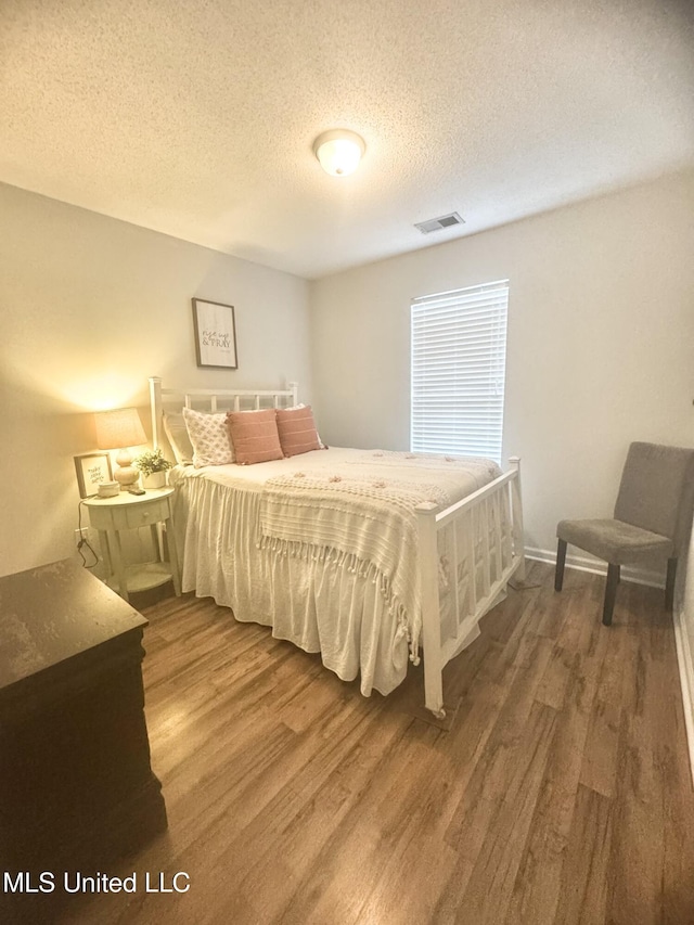 bedroom with visible vents, a textured ceiling, and wood finished floors