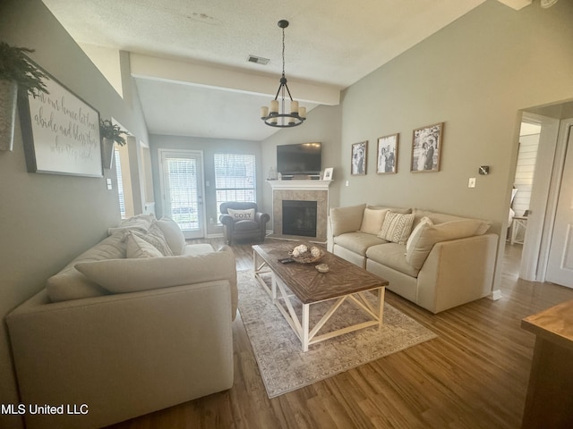 living area featuring vaulted ceiling with beams, a fireplace, wood finished floors, visible vents, and an inviting chandelier