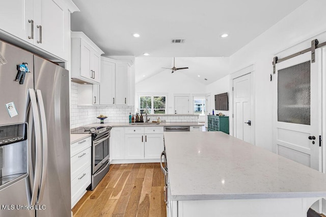 kitchen featuring appliances with stainless steel finishes, vaulted ceiling, a kitchen island, and white cabinets