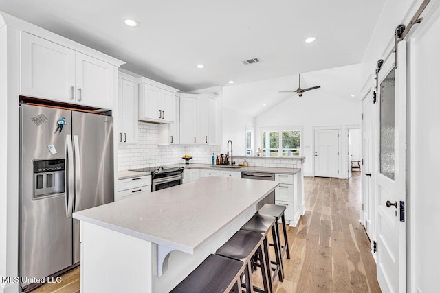 kitchen with vaulted ceiling, white cabinets, a kitchen breakfast bar, stainless steel appliances, and a barn door