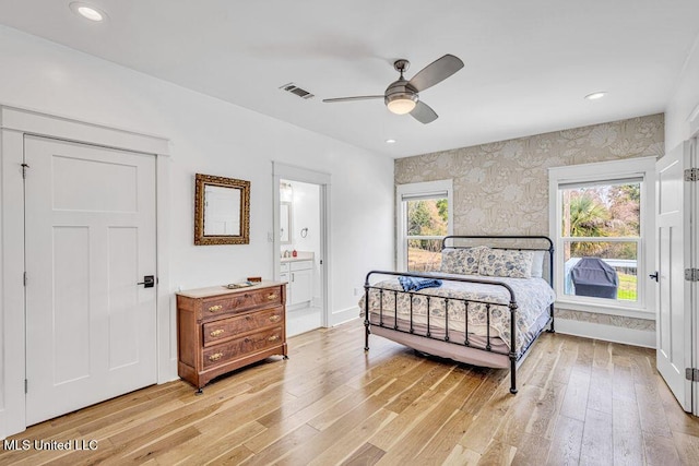 bedroom with multiple windows, ceiling fan, light wood-type flooring, and ensuite bath