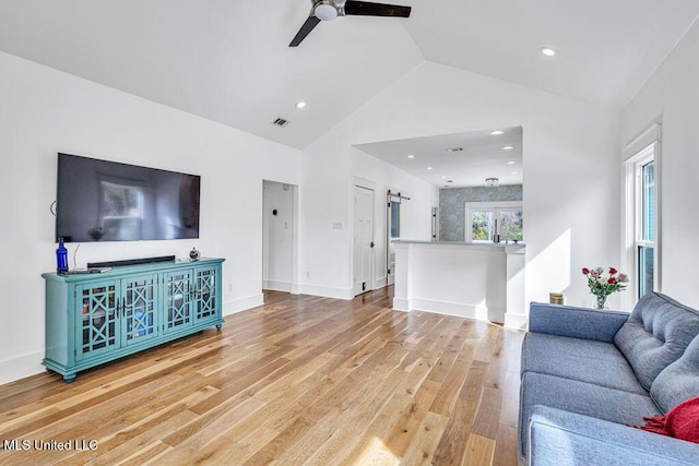 living room with vaulted ceiling, a barn door, hardwood / wood-style floors, and ceiling fan