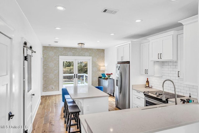 kitchen with light hardwood / wood-style flooring, a breakfast bar, white cabinetry, stainless steel appliances, and a barn door